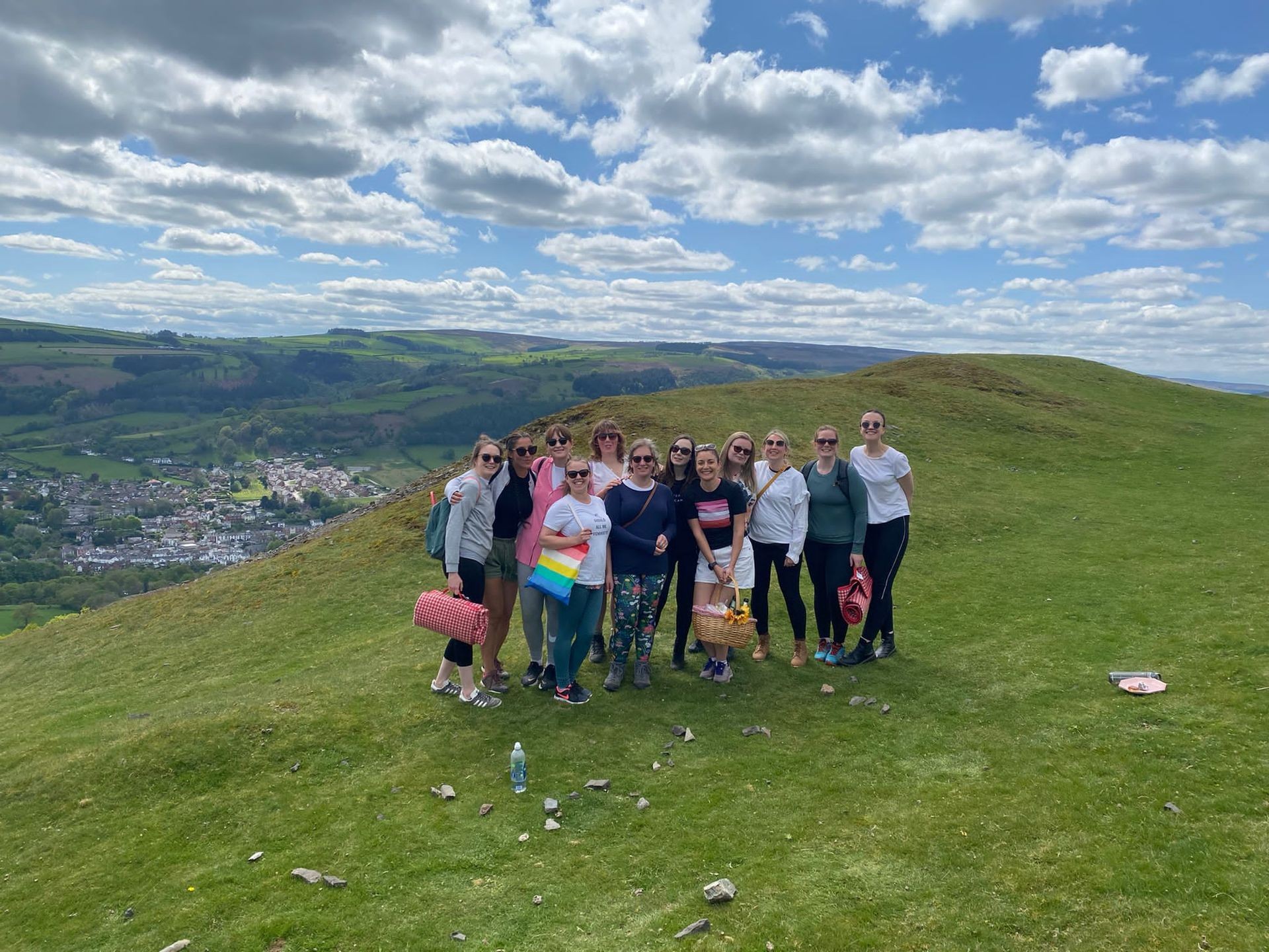 Group of people standing together on a scenic hillside with a village and rolling hills in the background.